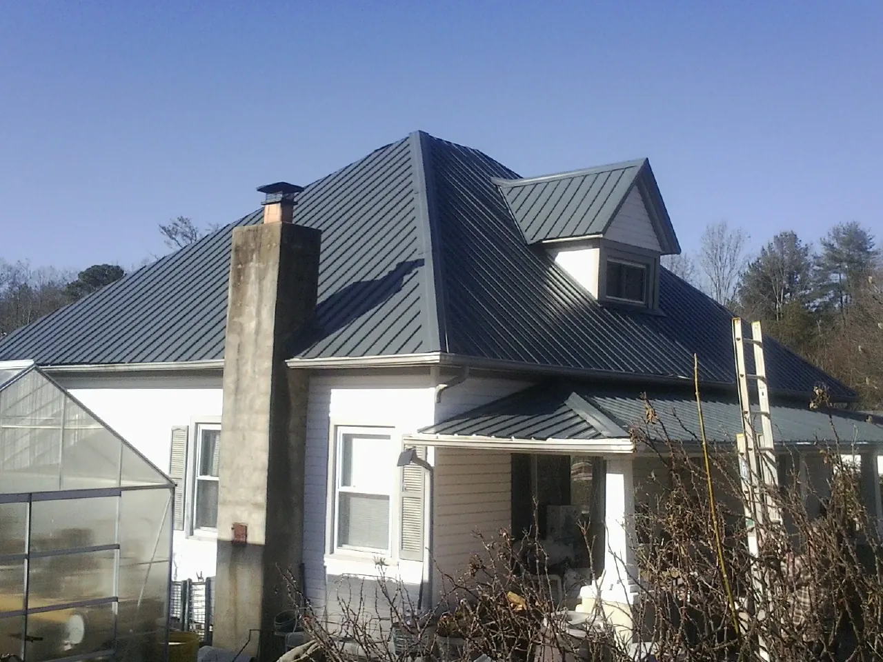 Dark blue standing seam metal roof on a white farmhouse with dormer — Slate & Tile Roof Repair by Roofing Brothers in Sachse