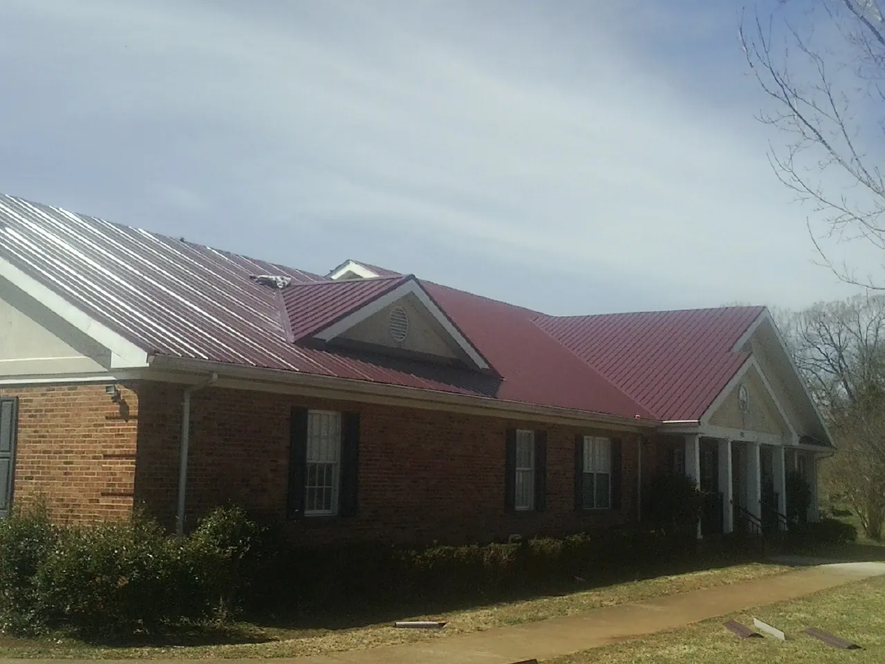 Red metal roof with gabled entries on a long brick building, from a Hail Damage Roof Repair job in Sachse