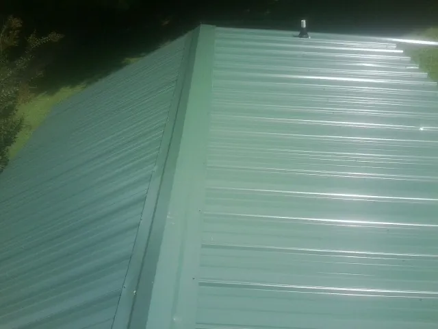 New green metal panels meeting at the ridge of a roof — Flat Roof Repair work by our crew in Sachse