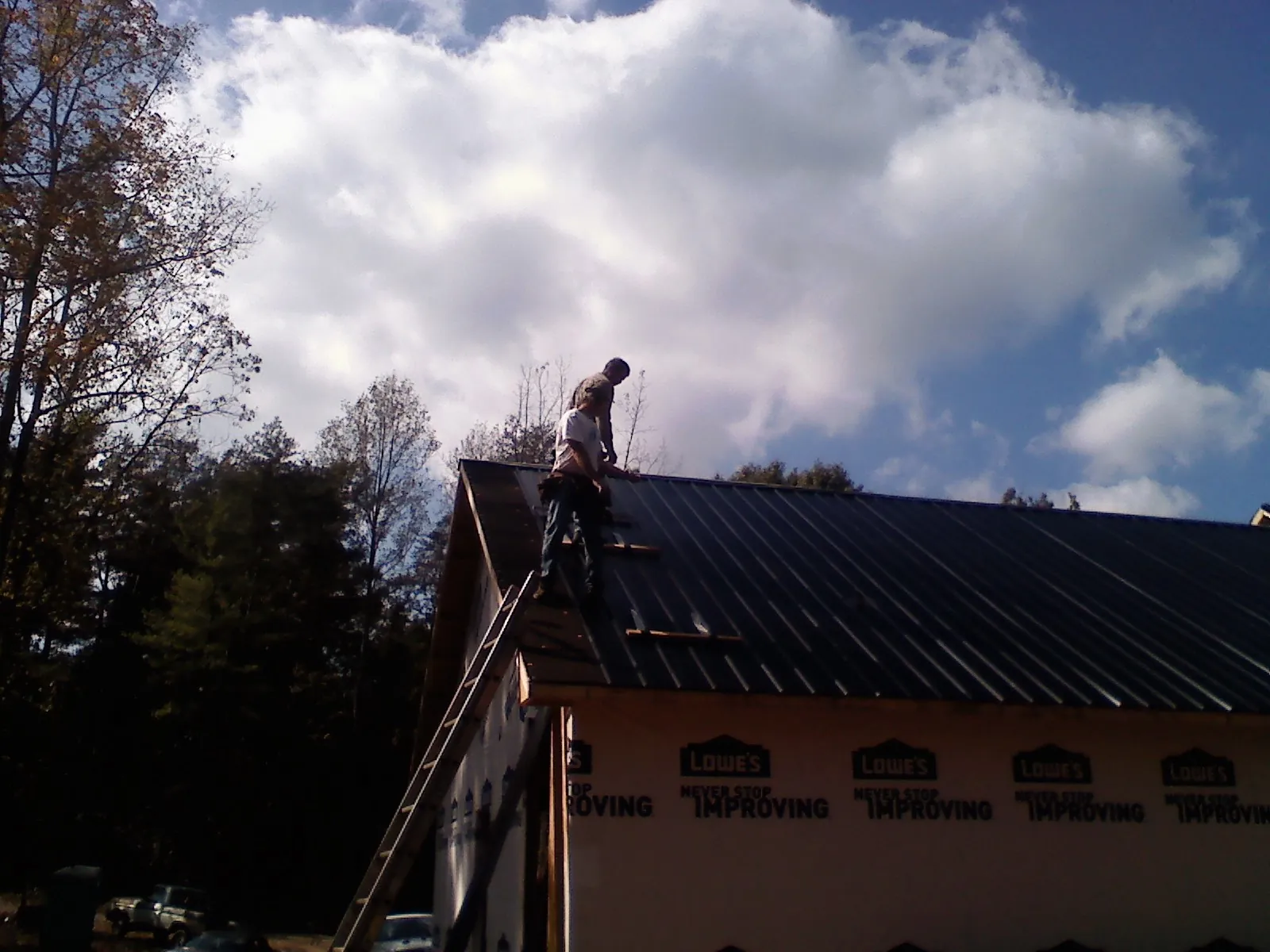 Roofer fastening dark metal panels high against a cloudy sky, from a Roof Inspection job in Sachse