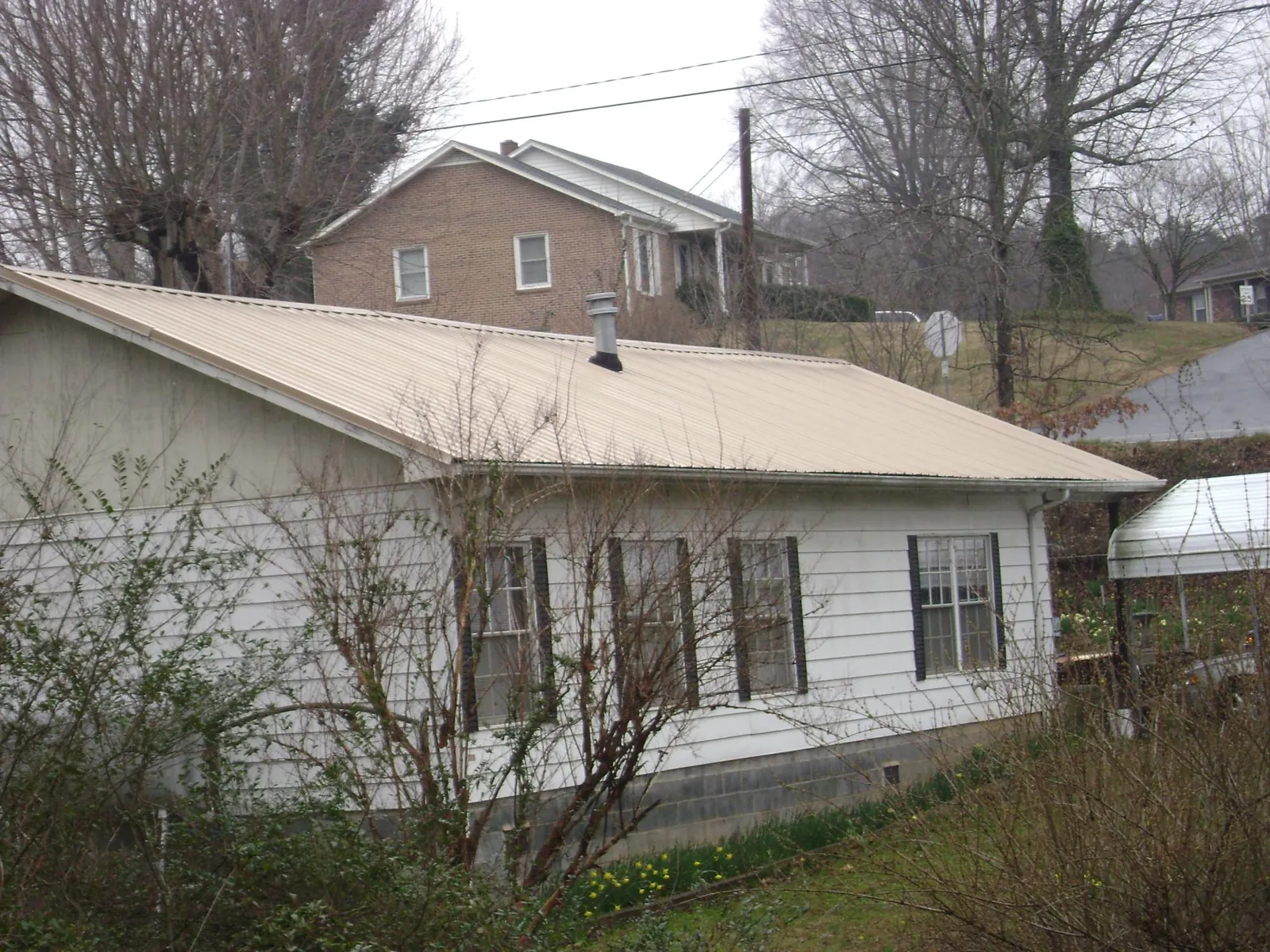 Tan metal roof on a white sided house set into a hillside — Commercial Roofing by Roofing Brothers in Sachse